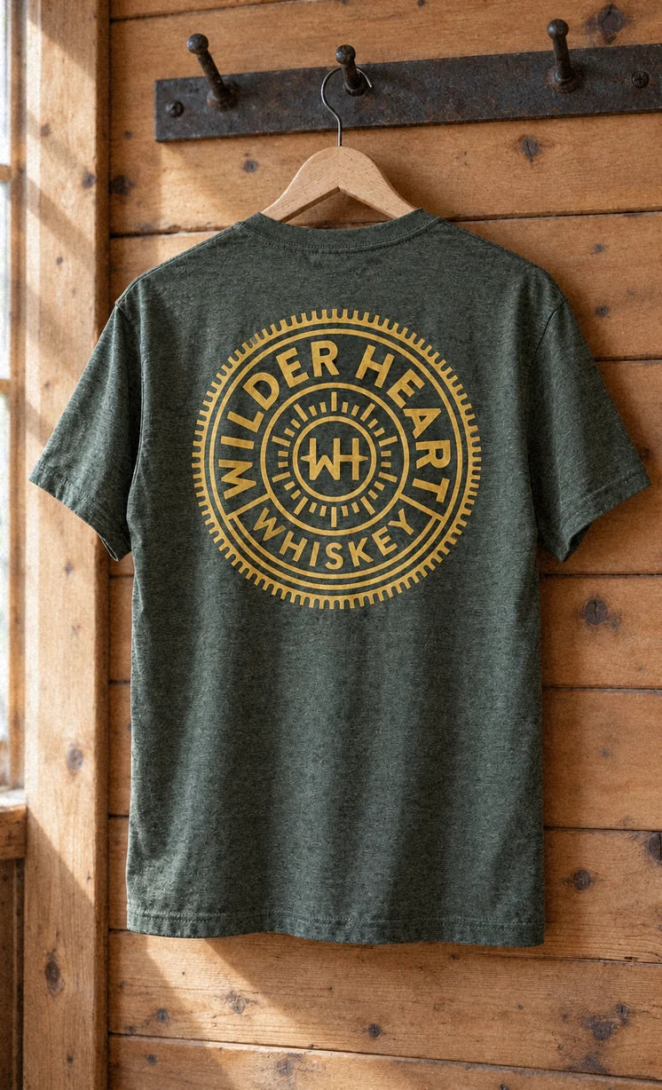 The Military Green tee on a hanger on a pine peg rail, the medallion on the back