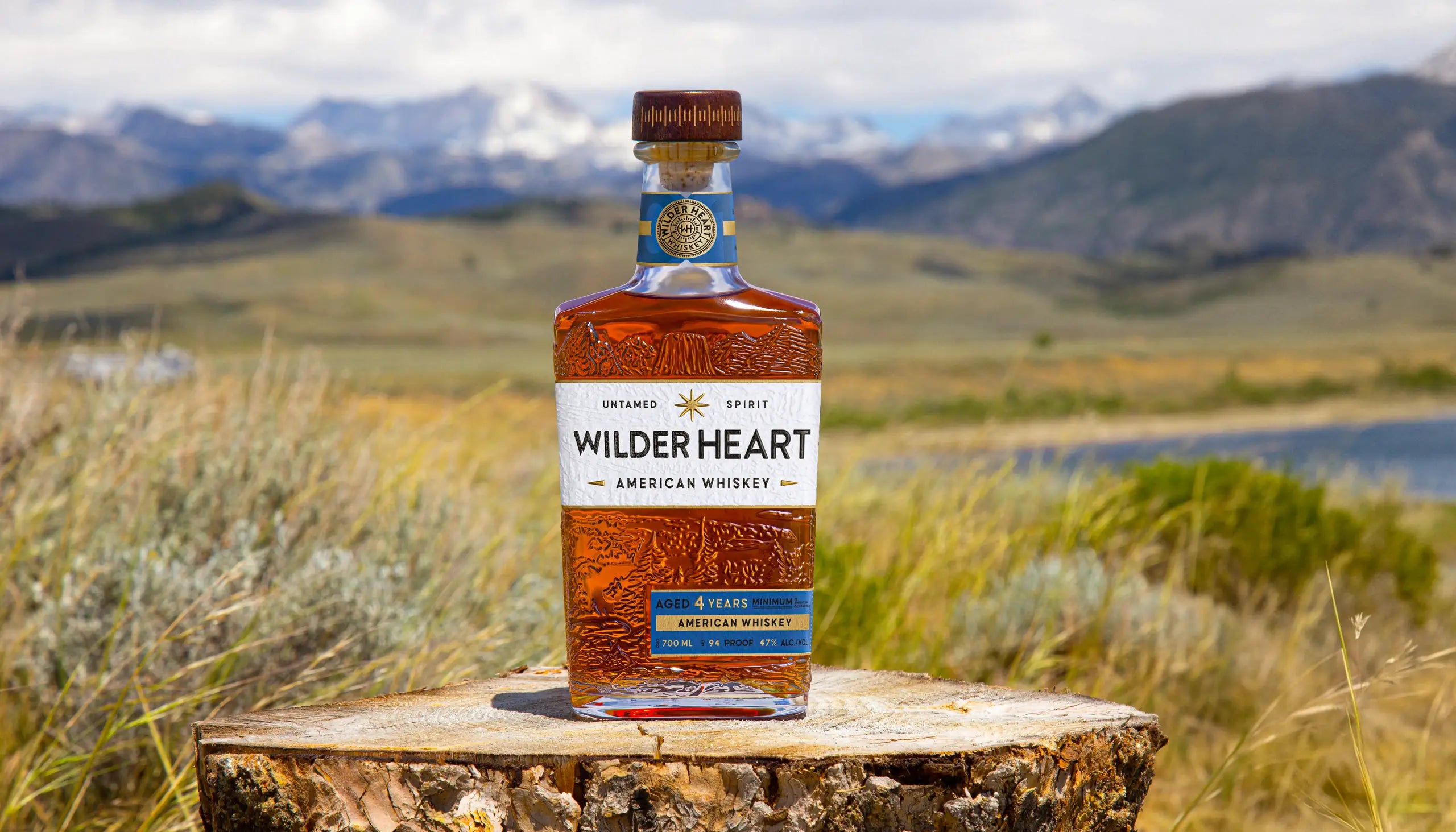 A bottle of Wilder Heart on a stump in a mountain meadow