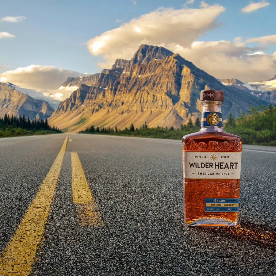 A bottle of Wilder Heart on an empty mountain road, peaks and cloud behind